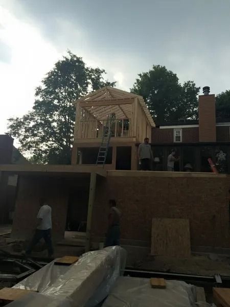 Construction site with workers, wooden framing. New second story being built on an existing structure. Cloudy sky.