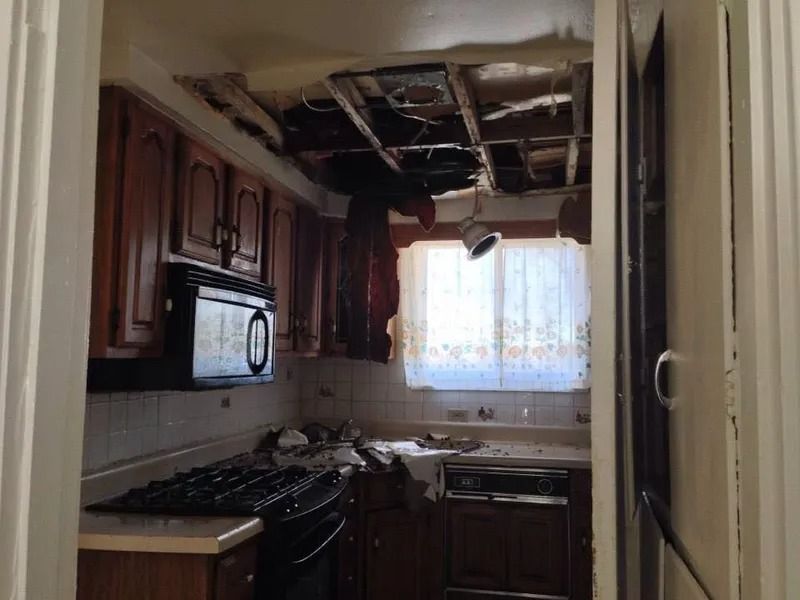 Kitchen with significant ceiling damage, cabinets, appliances, and debris visible.