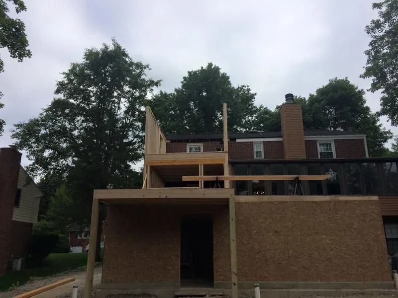 Construction of a two-story addition to a building; plywood siding, framed walls, and supporting beams visible.