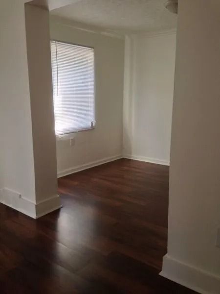 Empty room with dark wood floor, white walls, and a window with blinds.