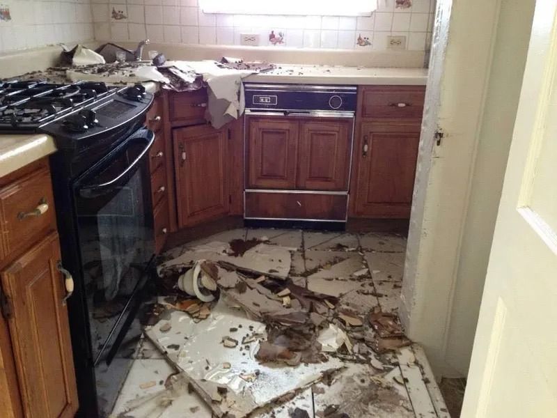 Damaged kitchen with debris on the floor and damaged cabinets. Black stove on the left.