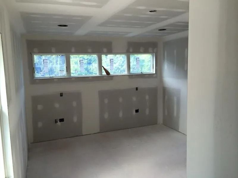 Interior room under construction; drywall on walls, windows, recessed ceiling lighting.