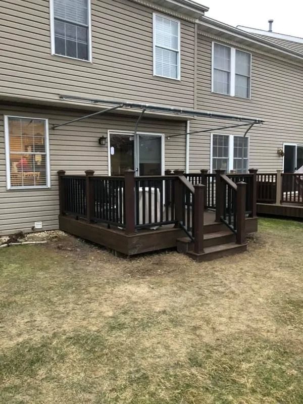 Backyard deck with dark brown railing and stairs, facing a beige house with windows and a sliding glass door.