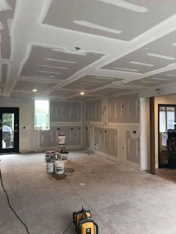 Room under construction with drywall installed on walls and ceiling. Buckets sit on the concrete floor.