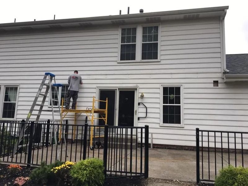 Man on scaffolding painting white siding of a two-story house.