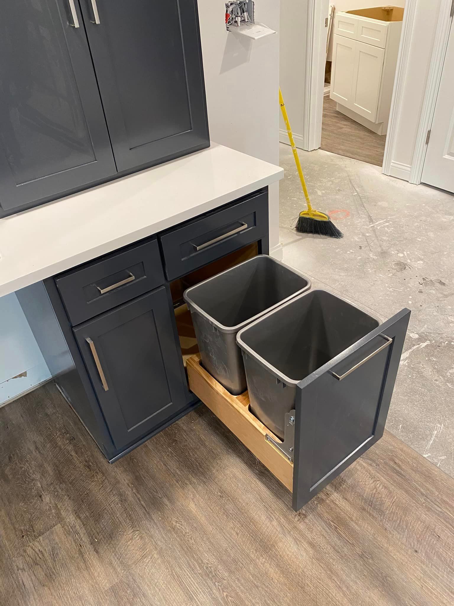 Two trash cans are pulled out of a drawer in a kitchen.