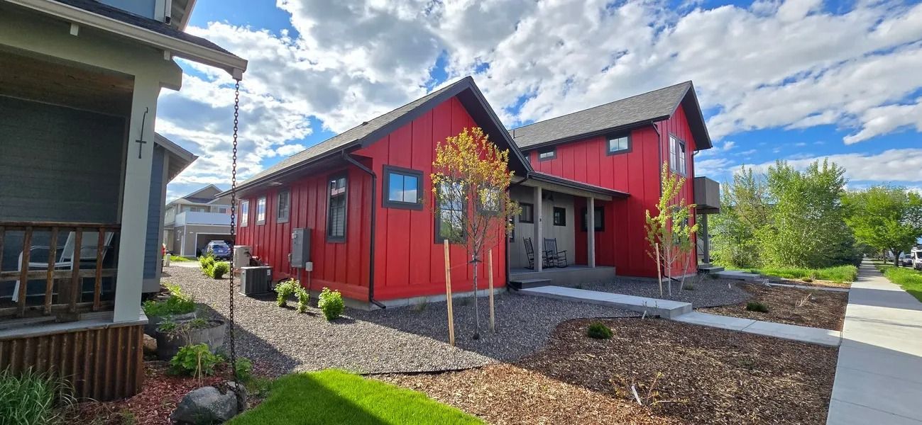Red modern homes with front yards, bright blue sky, and a sidewalk.