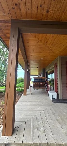 Wooden porch with posts, planks, and ceiling. A bench and white container sit in the distance.