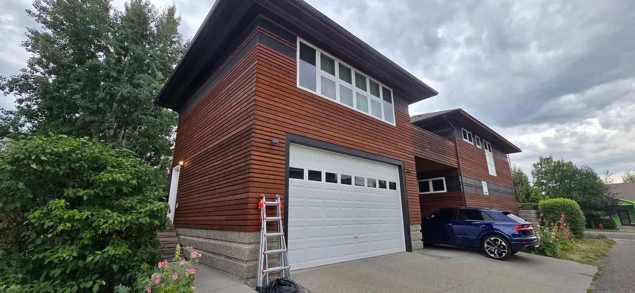 Brown two-story house with white garage door and blue car parked in driveway. Cloudy sky.