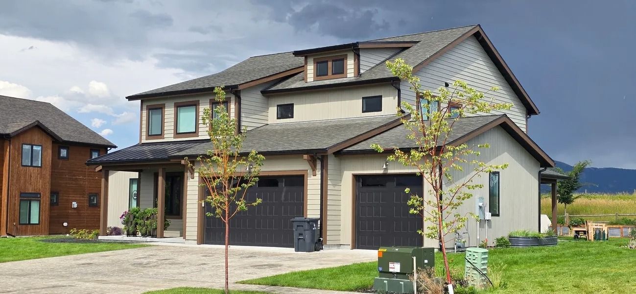 Modern two-story house with gray roof, tan exterior, and two-car garage under a cloudy sky.