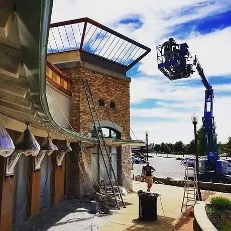Construction workers on a building, using a lift and ladder. The building has brick and is under renovation.