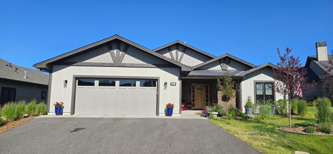 A gray single-story house with a blue sky.  A driveway leads to a gray garage door.  Blue flower pots.