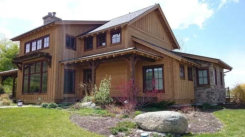 Wooden house with stone accents and a sloped roof sits on a grassy lawn.