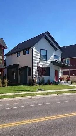 Two-story modern house with white siding and black roof and trim on a sunny day.