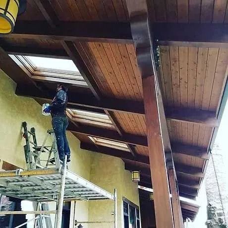 Person painting a wooden ceiling from a scaffold; building exterior.