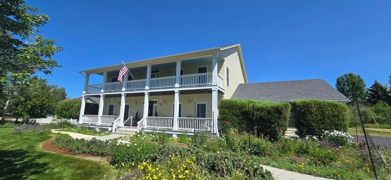 Two-story house with white trim and balconies, under a bright blue sky. An American flag is visible.