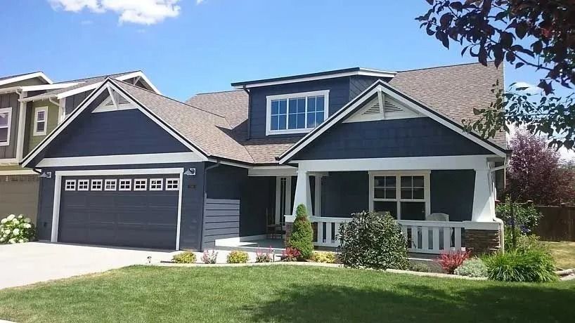 Blue-sided house with a porch and a garage on a green lawn with a clear blue sky.