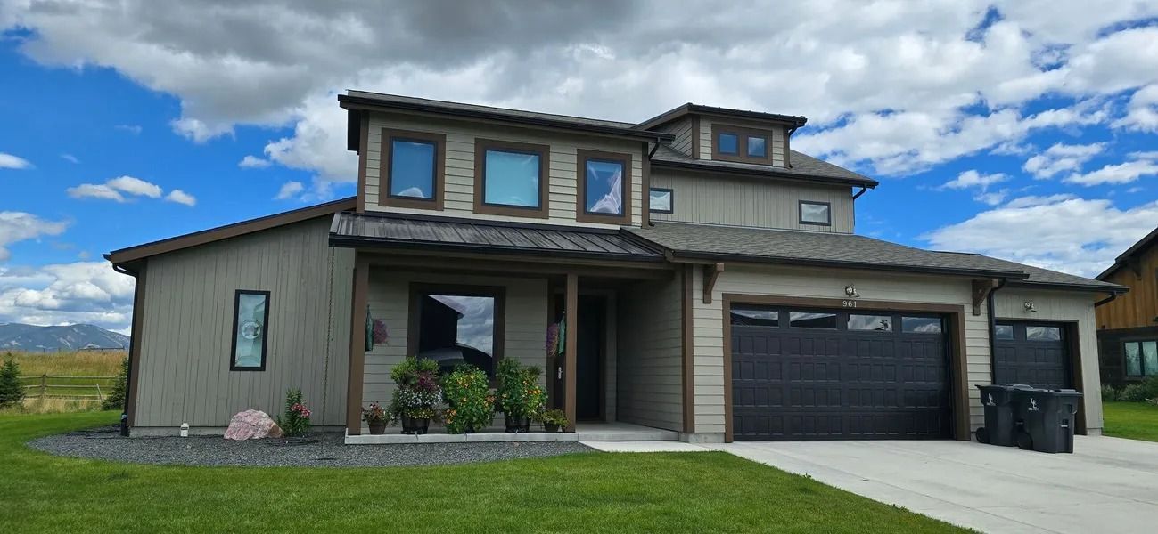 Modern house with dark garage doors, blue sky and green lawn.