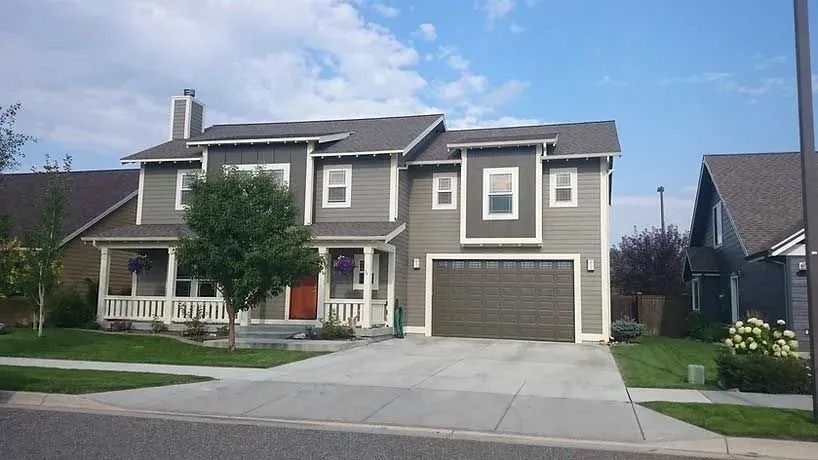 Two-story house with gray siding, a porch, and a garage, on a sunny day.