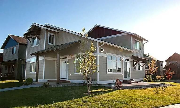Two-story modern house with covered porch, tan siding, and green lawn on a sunny day.