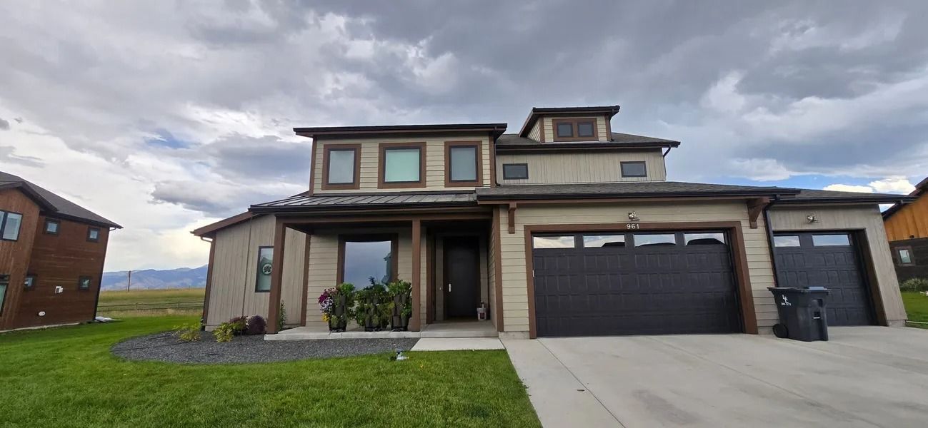 Modern two-story house with dark garage doors, green lawn, and cloudy sky.