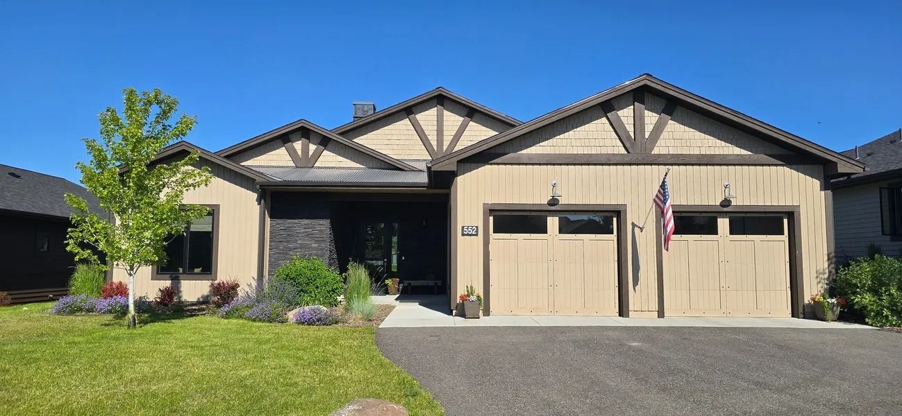 House exterior with tan siding, brown trim, and a blue sky. There is a flag hanging next to the garage.