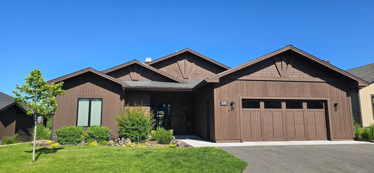 Brown house with wood siding, green lawn, and blue sky.