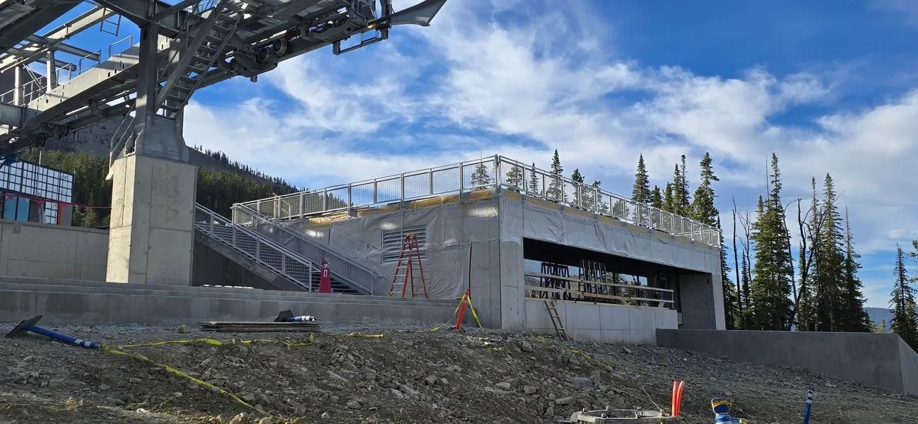 Construction site with concrete structures, ski lift infrastructure and a bright sky with trees.