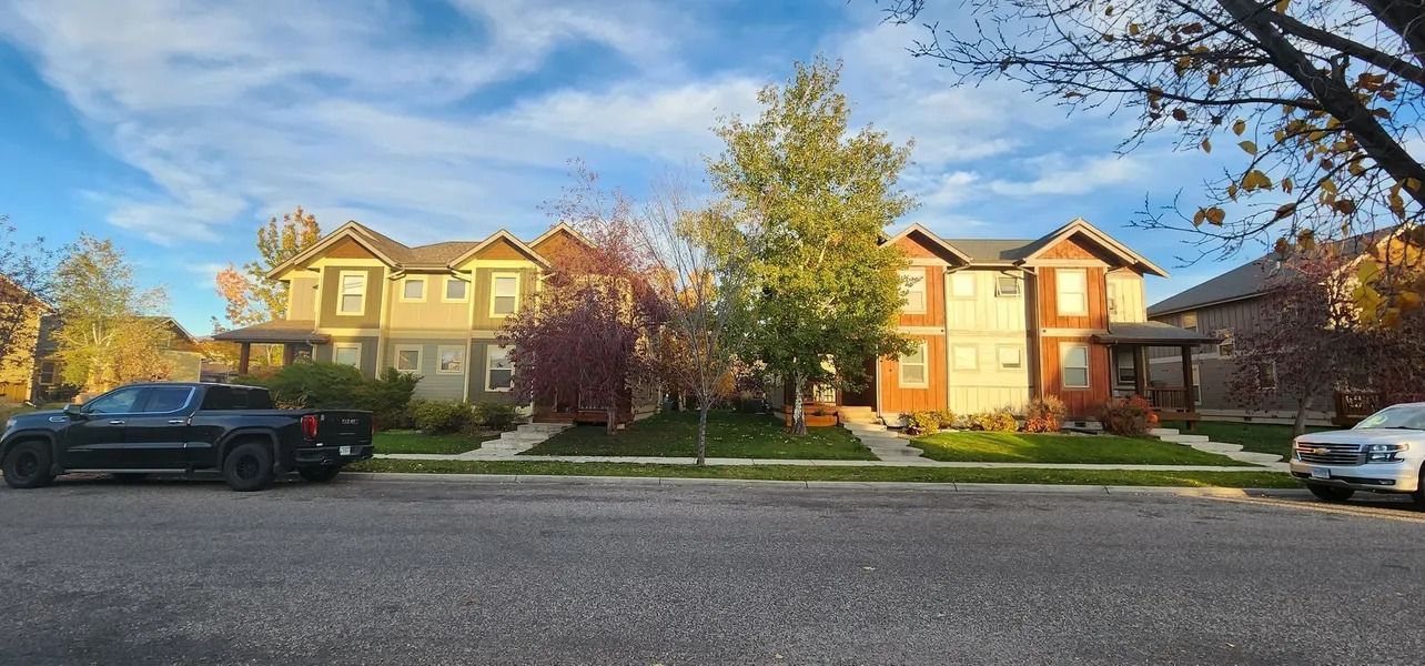 Row houses on a street under a blue sky, with cars parked in front.