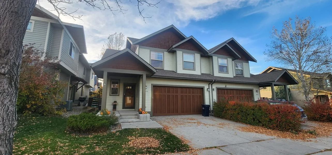 Townhomes with brown garage doors, beige siding, and brown trim on a partly cloudy day.