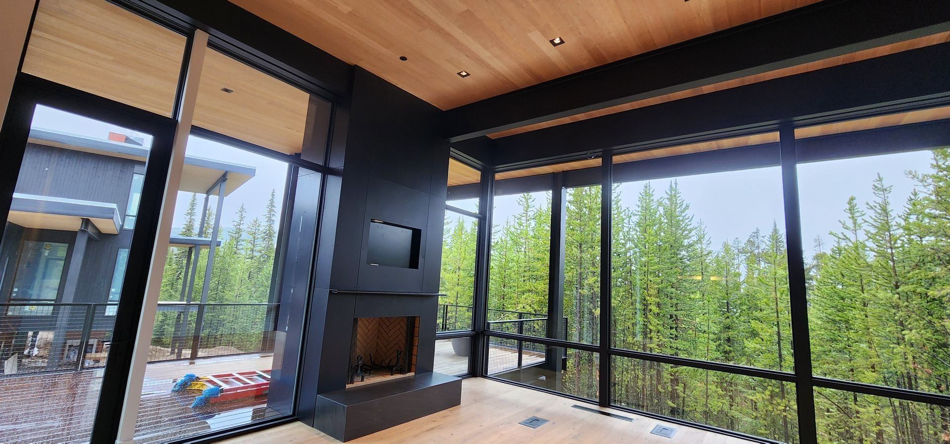 Modern living room with floor-to-ceiling windows overlooking a forest and a fireplace.
