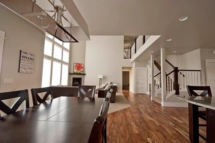Spacious modern interior with dining table, fireplace, and second-floor balcony. Wooden floors, white walls, and bright windows.