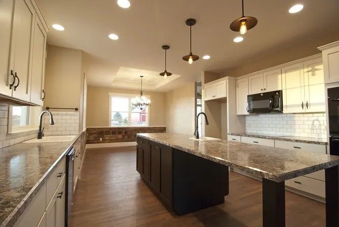 Modern kitchen with dark island and granite countertops, light cabinets, and pendant lights.