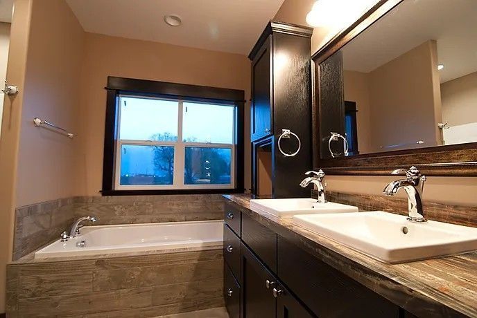 Bathroom with a bathtub, double sinks, dark cabinets, and a window.