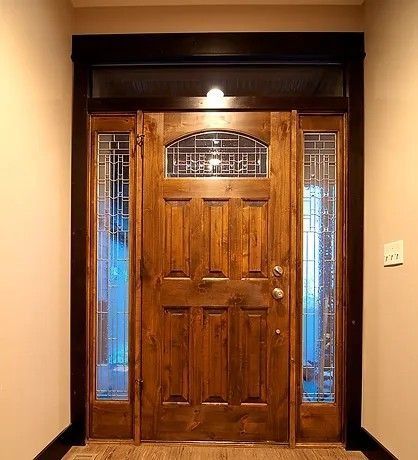 Wooden front door with glass sidelights and transom, brown trim, and interior light.