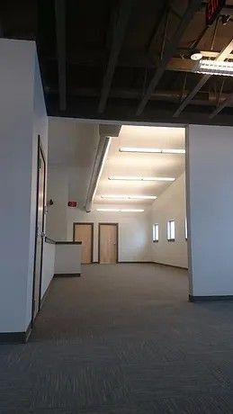 Empty office space with gray carpet, white walls, and exposed ceiling beams.