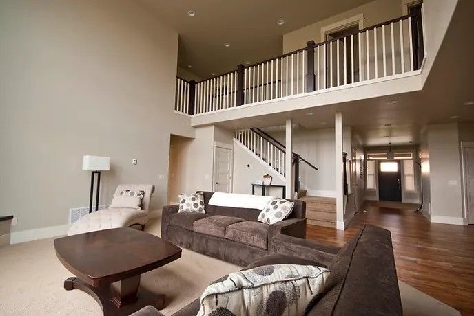 Spacious living room with brown couches, balcony, staircase, and light beige walls.