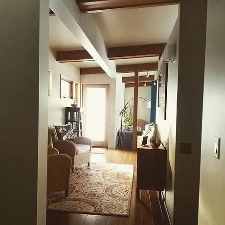 Hallway with wooden beams, chairs, patterned rug, and a door leading outside.