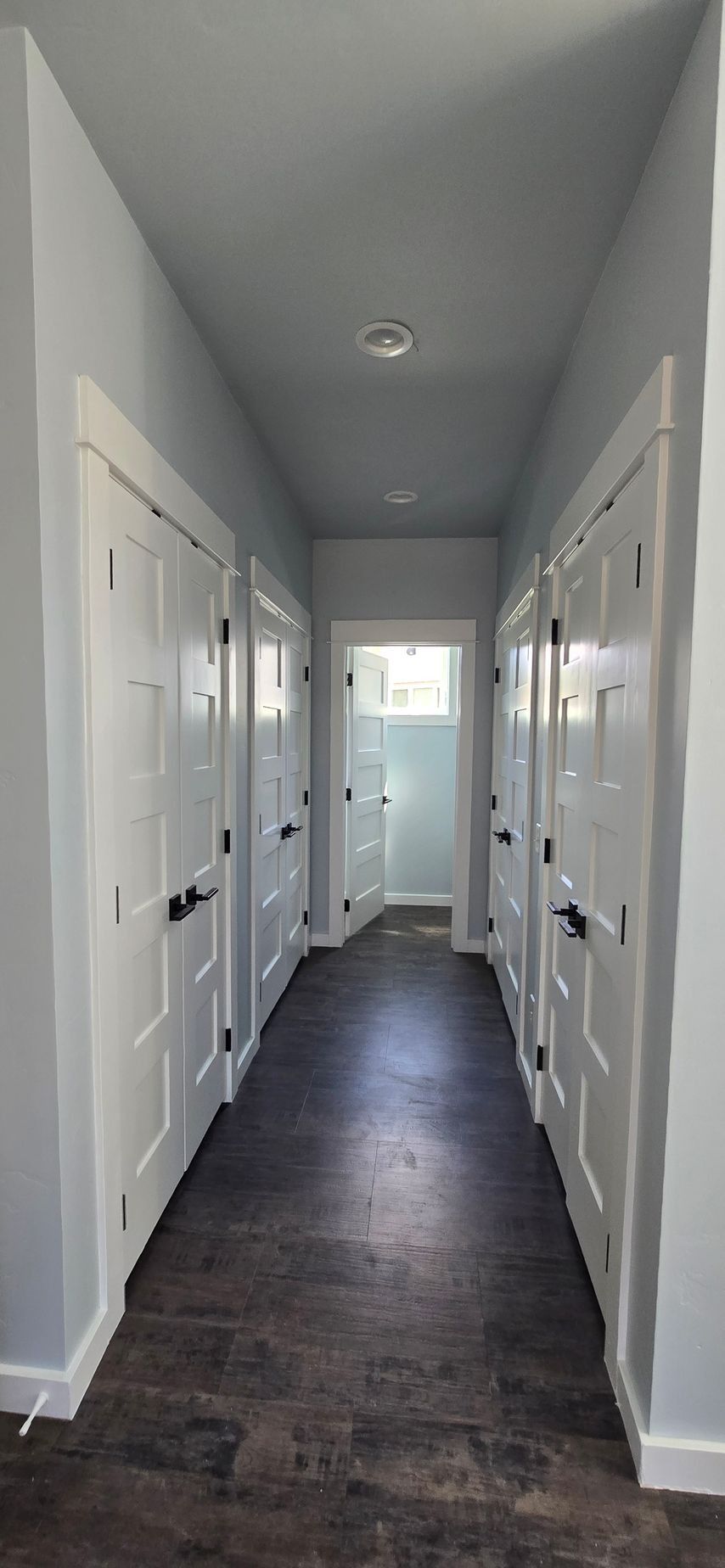 A long hallway with white doors on both sides, leading to a frosted glass door at the end. Dark flooring.