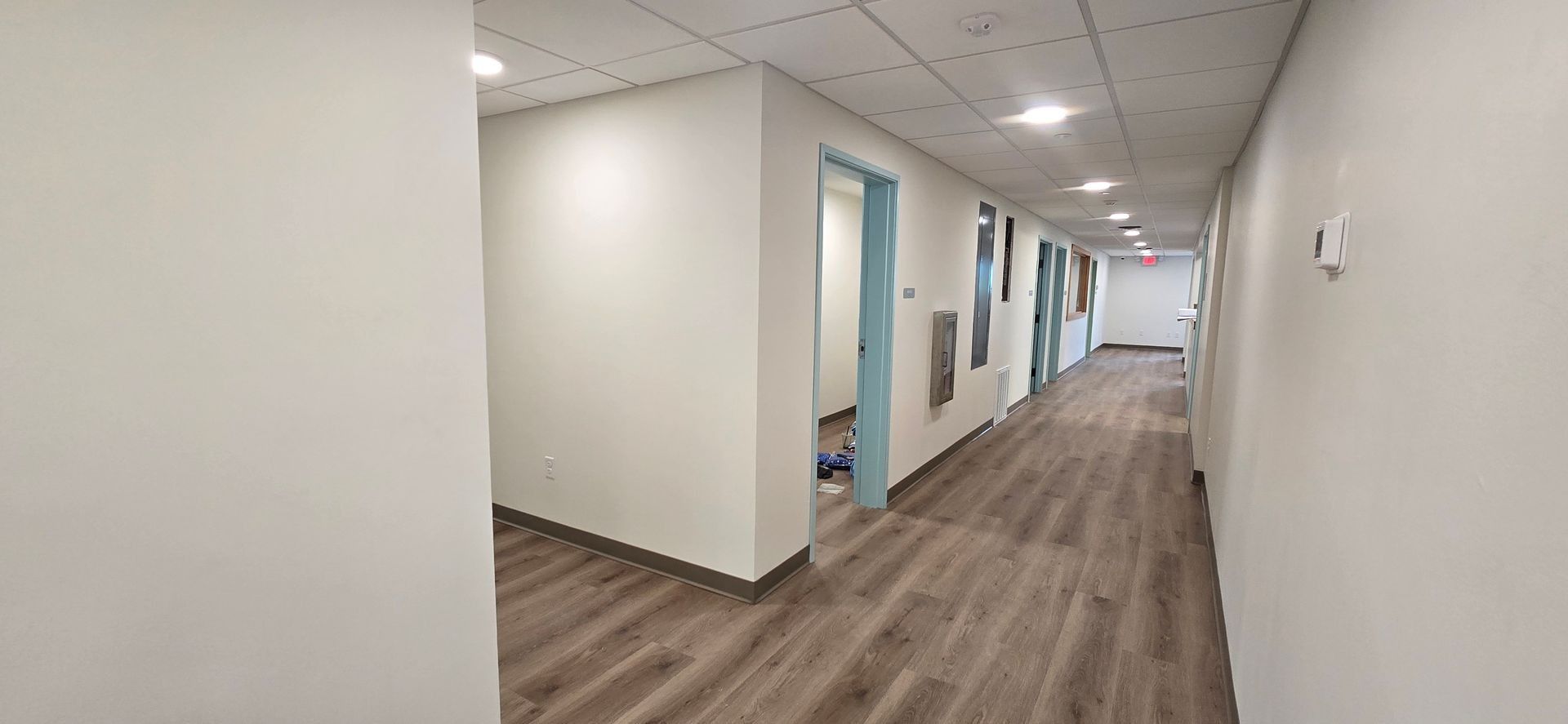 A long, bright hallway with several closed doors and wooden flooring.