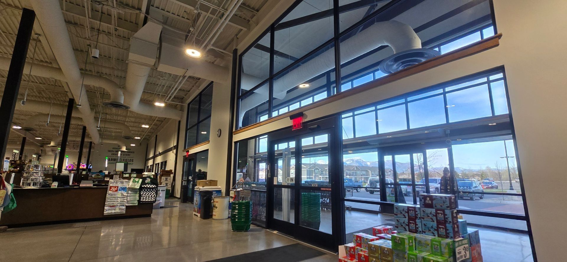 Interior view of a grocery store entrance with glass doors, tall windows, and a high ceiling.