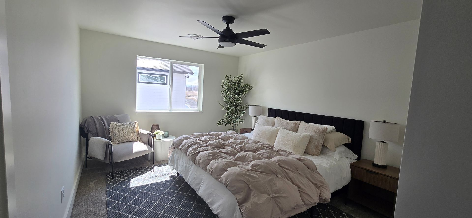 Bedroom with a bed, armchair, window, and ceiling fan. The room has light-colored walls and flooring.