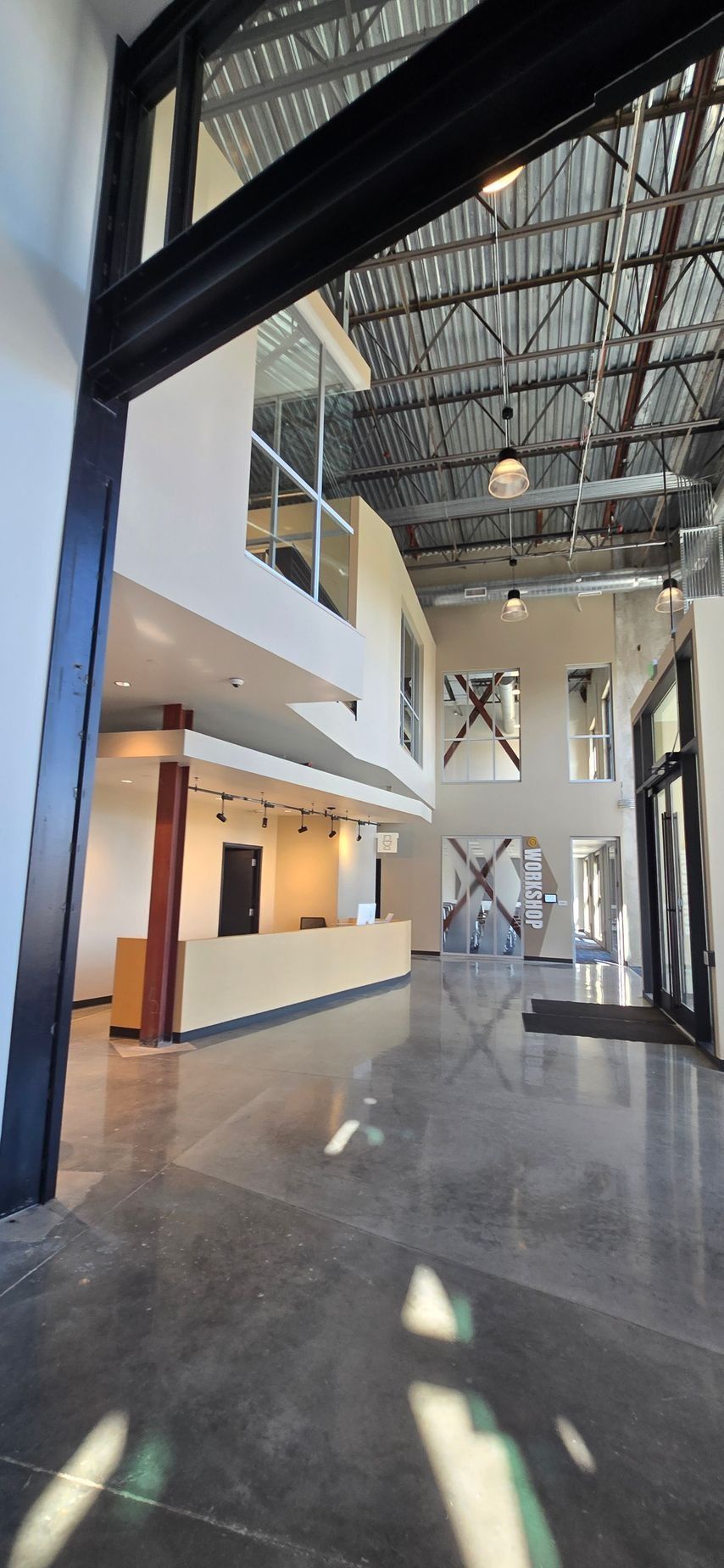 Interior of a modern building with a concrete floor, a reception desk, and exposed metal beams.