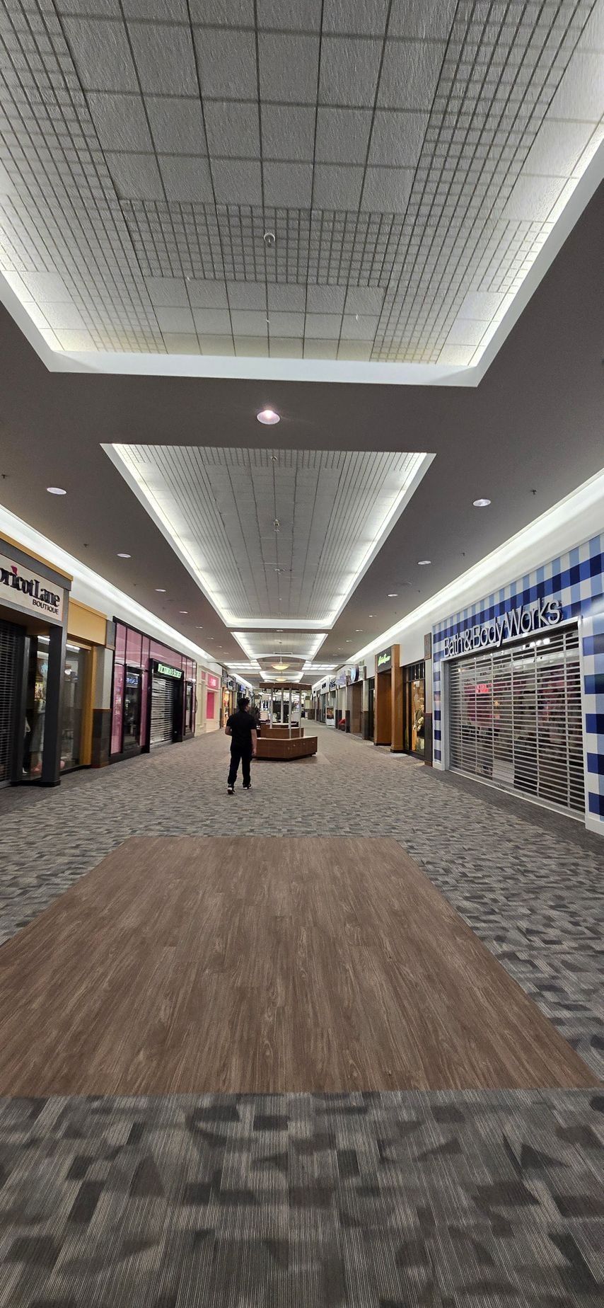 Long hallway in a shopping mall with stores on either side. A person walks down the hall.