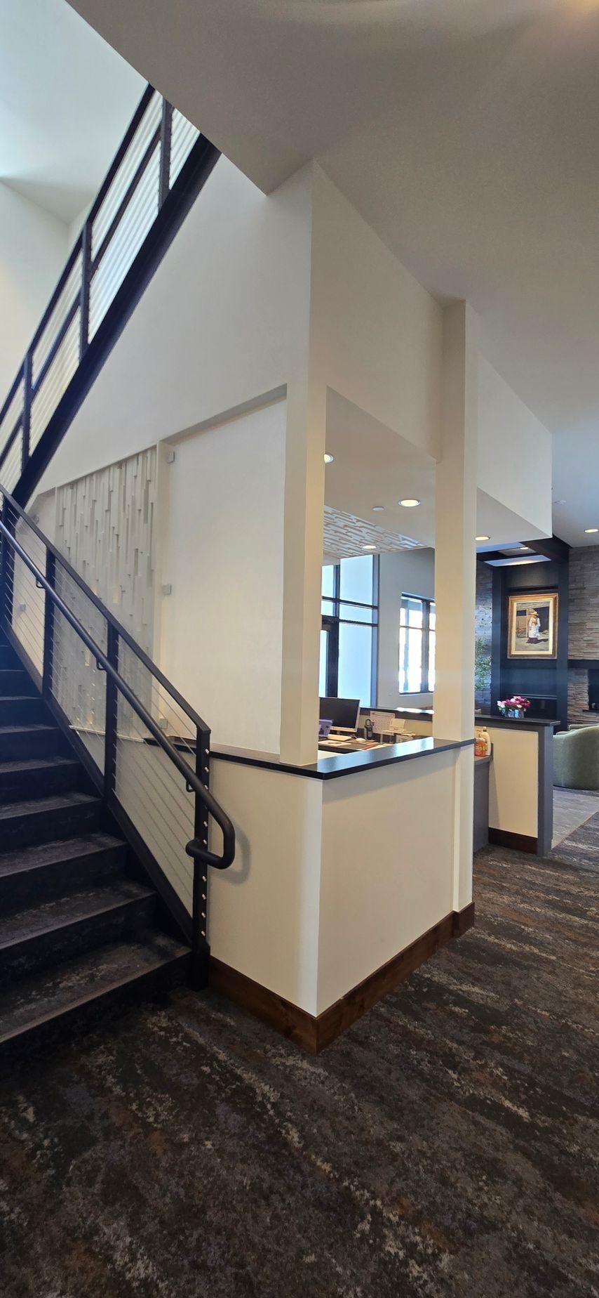 Staircase with black metal railing and dark stone flooring, leading to an open area with a counter.