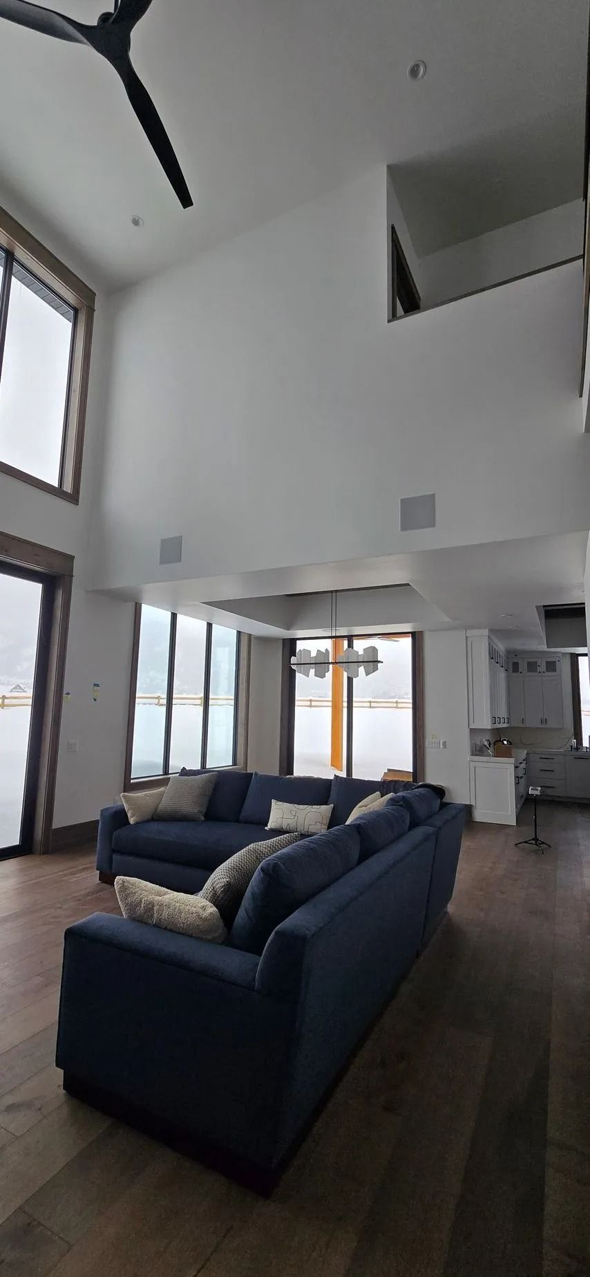 Modern living room with blue sectional, high ceilings, large windows, and hardwood floors.