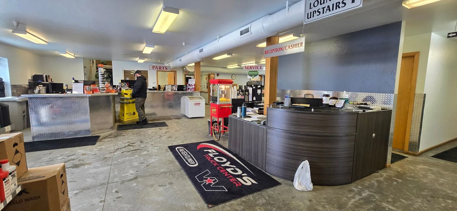 Interior of a store with counters, a rug, a person, and merchandise. Fluorescent lights illuminate the room.