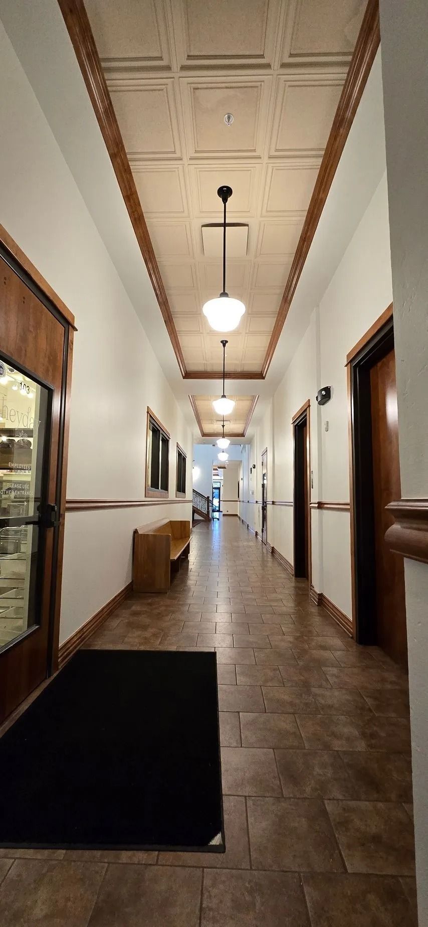 Long hallway with doors, a bench, and ceiling lights.