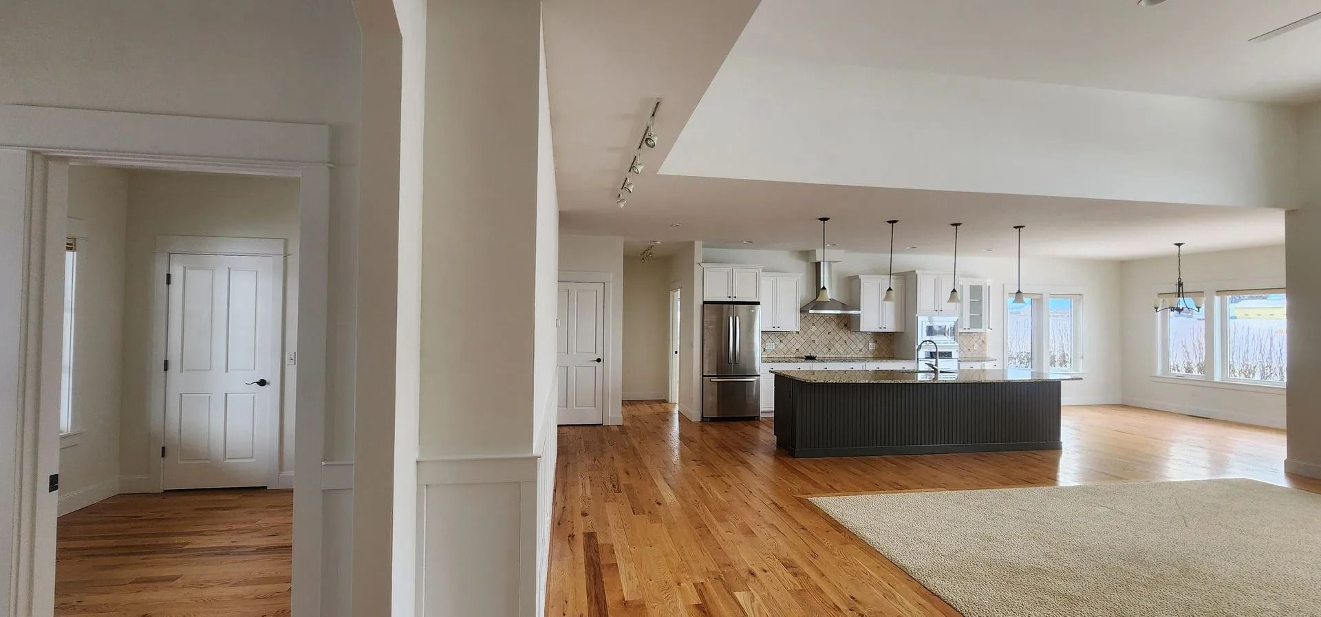Open-concept home interior with hardwood floors, a kitchen island, and a large rug.