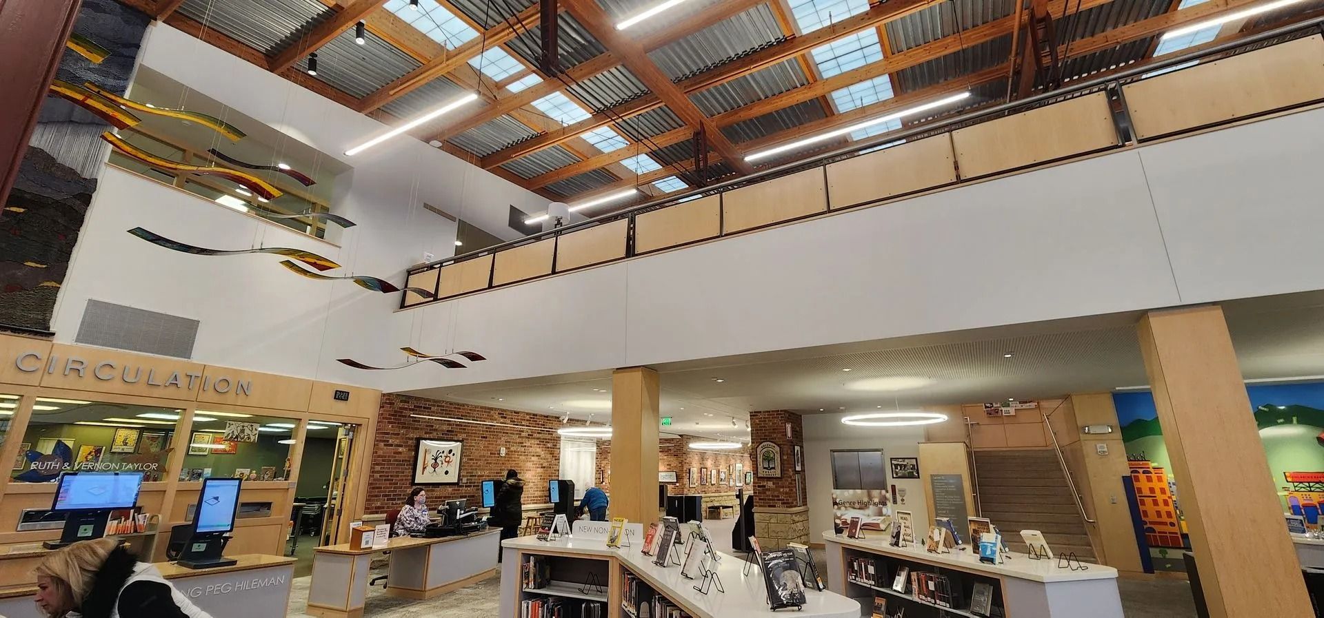 Interior view of a library with a mezzanine, high ceilings, wooden beams, and a circulation desk.